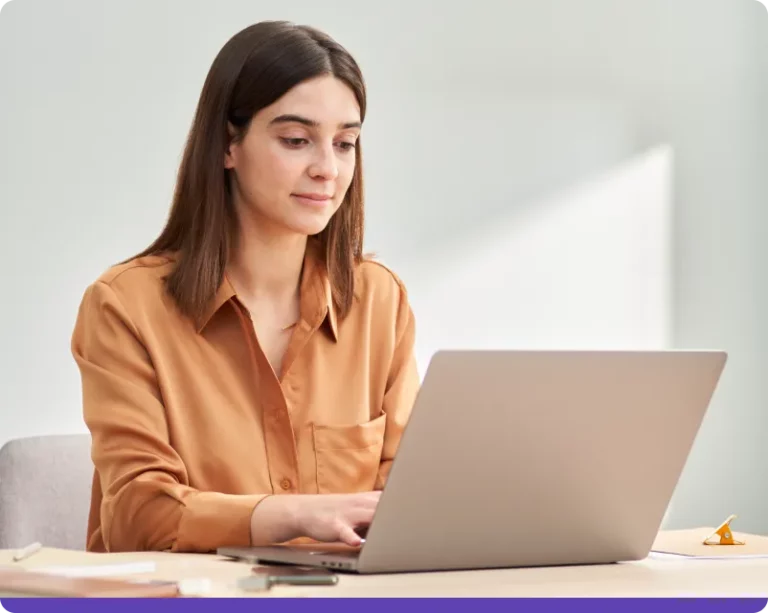 Woman with orange shirt typing on laptop.