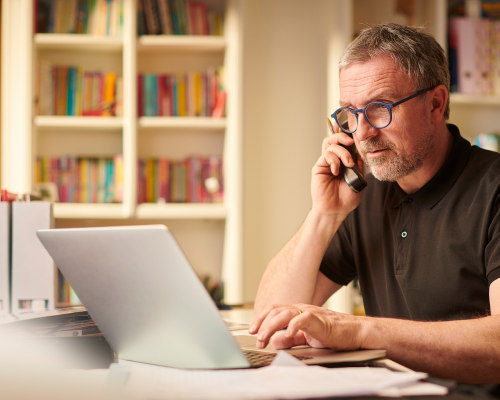 Man on the phone next to his computer calling a company to return a product. 